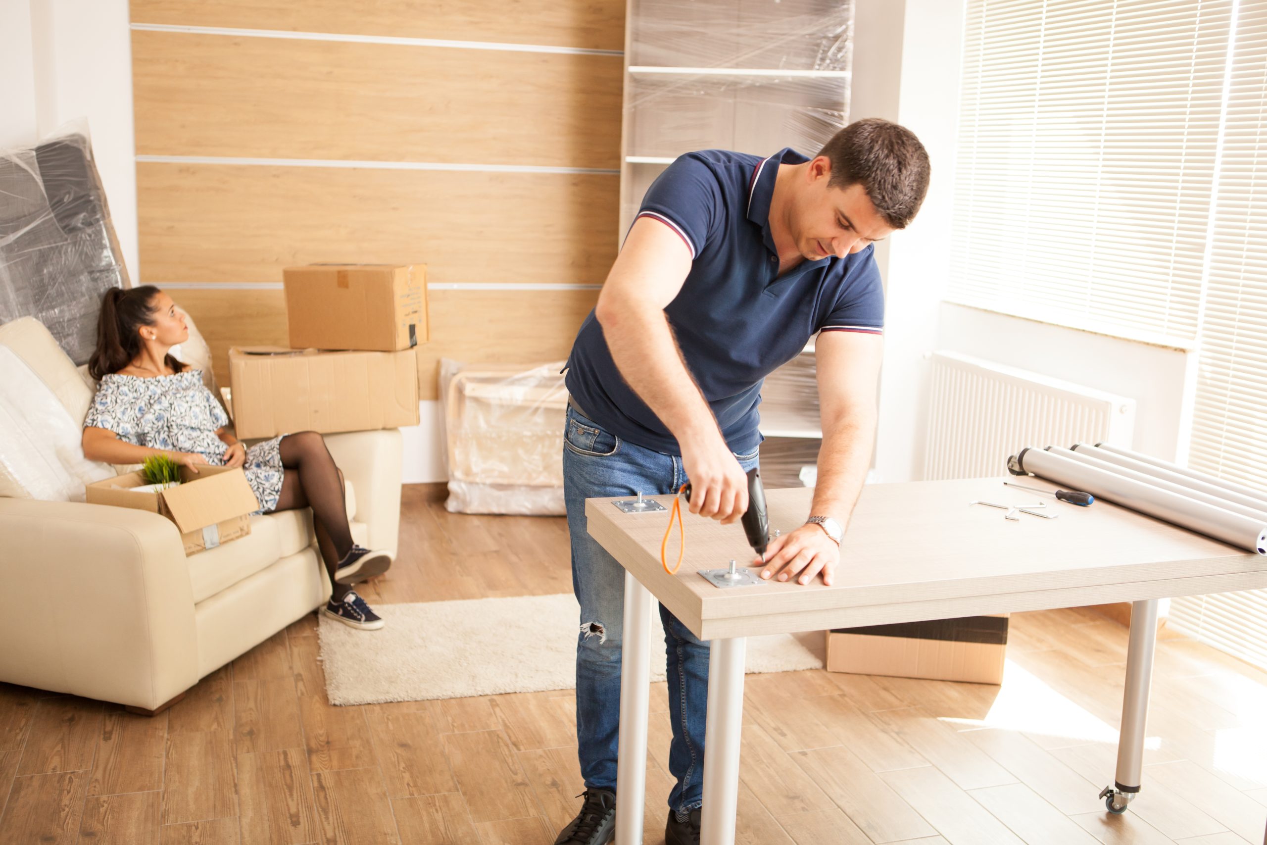 smiling man putting together self assembly furniture new home furniture new house scaled Flooring Companies